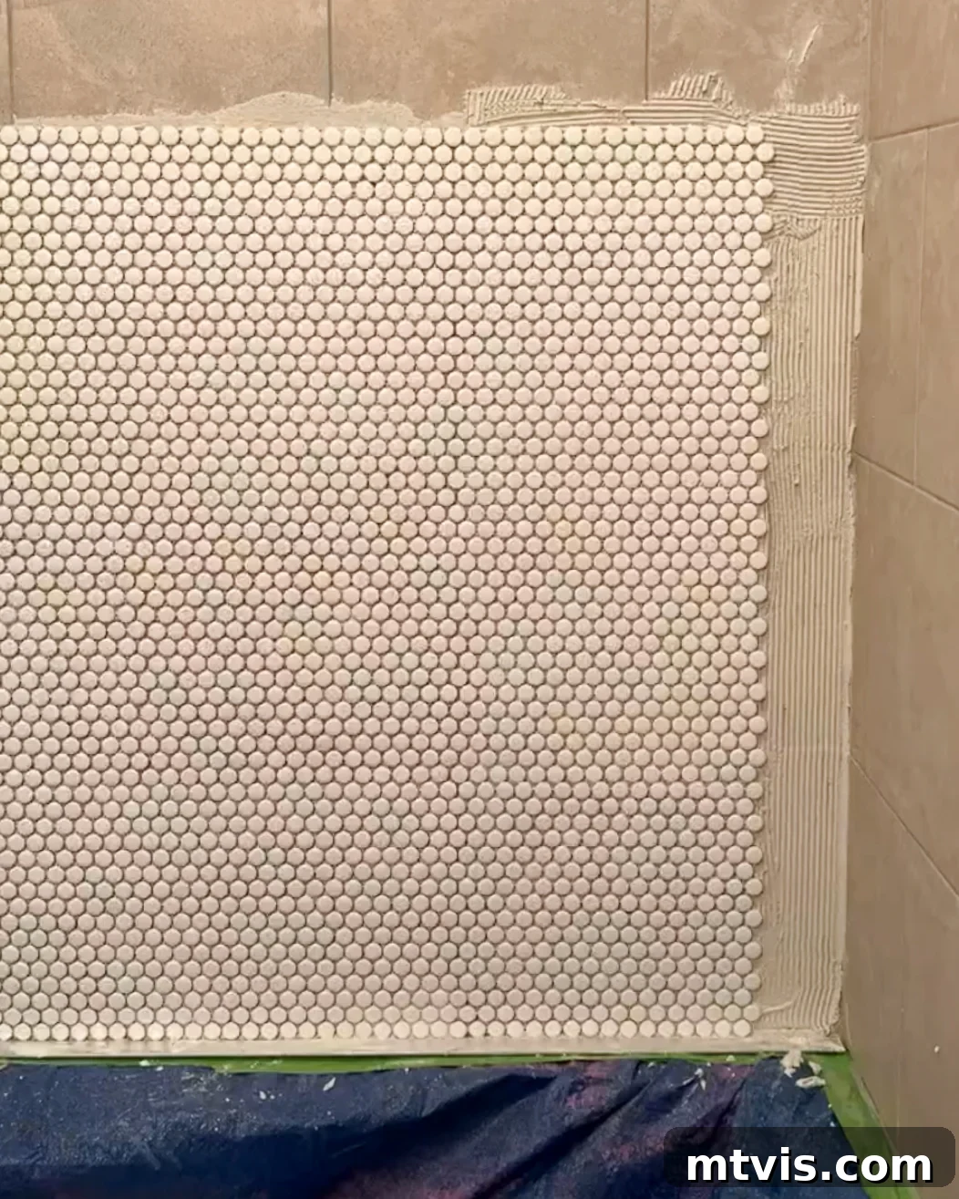 DIYer installing penny tiles over existing tiles in a shower, demonstrating the tile installation process