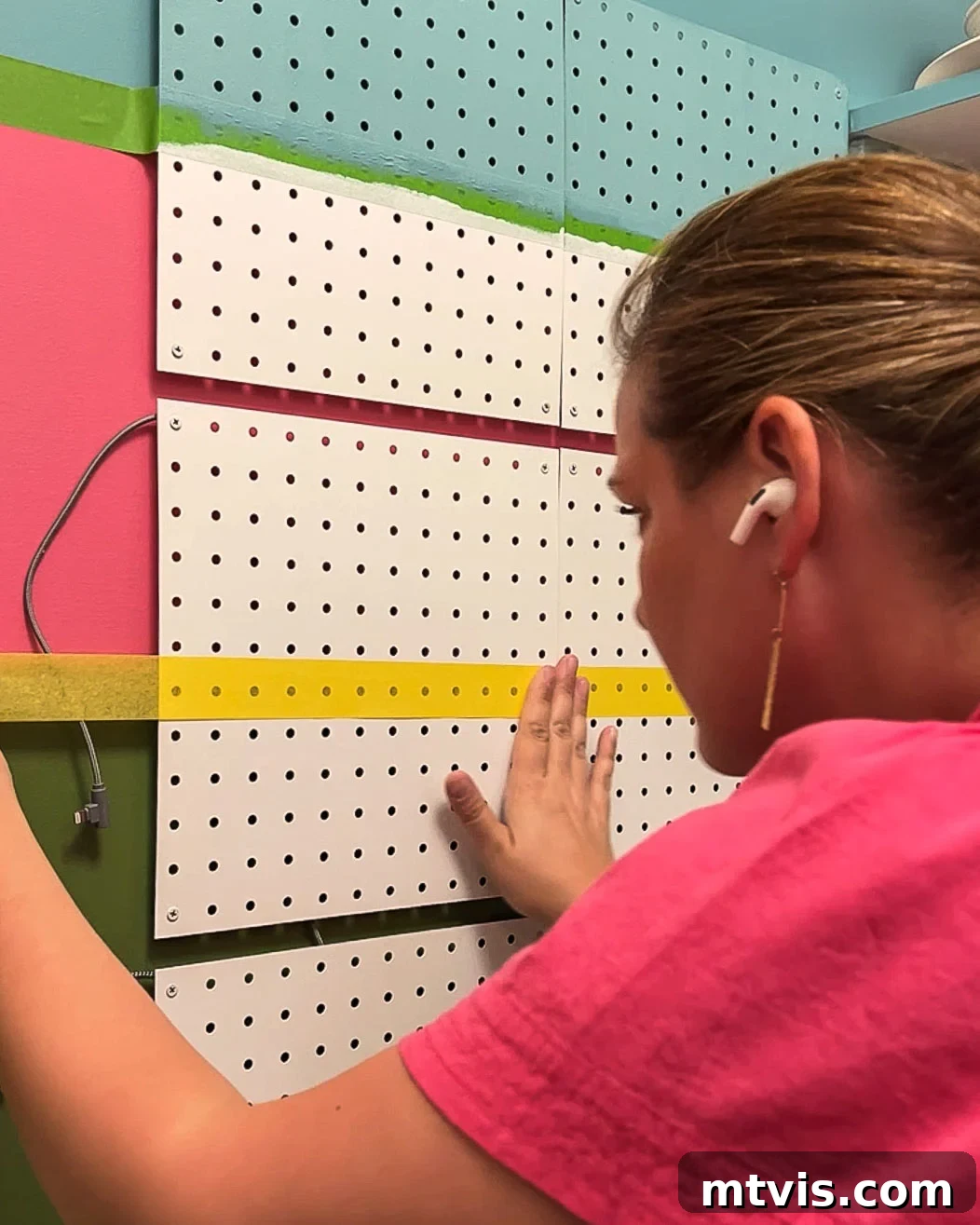 Woman painting stripes on metal pegboard panels to customize the family charging station