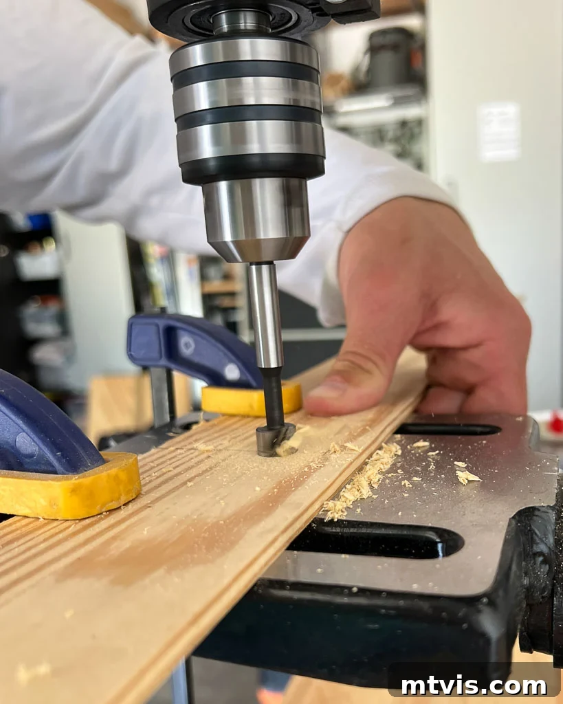 A Forstner bit drilling a perfectly sized recess into a wooden strip, preparing it for magnet insertion in a DIY poster hanger.