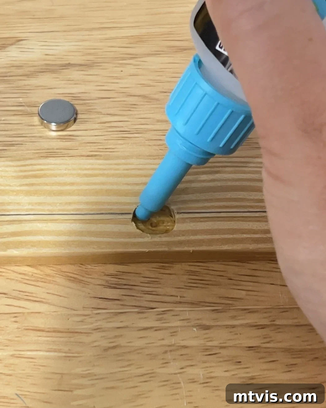 Close-up of small round magnets being glued into recesses on a wooden strip using adhesive for DIY magnetic poster hangers.