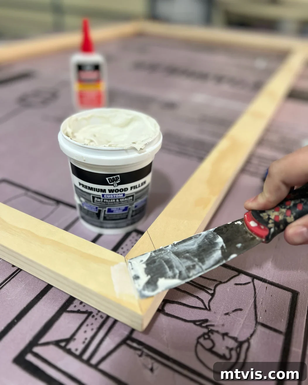 Filling miter joints with wood filler to achieve a smooth finish on the DIY TV frame