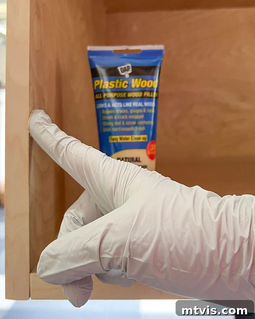 A hand expertly filling imperfections in a plywood DIY dog crate with DAP Plastic Wood all-purpose wood filler, ensuring a smooth, natural finish.