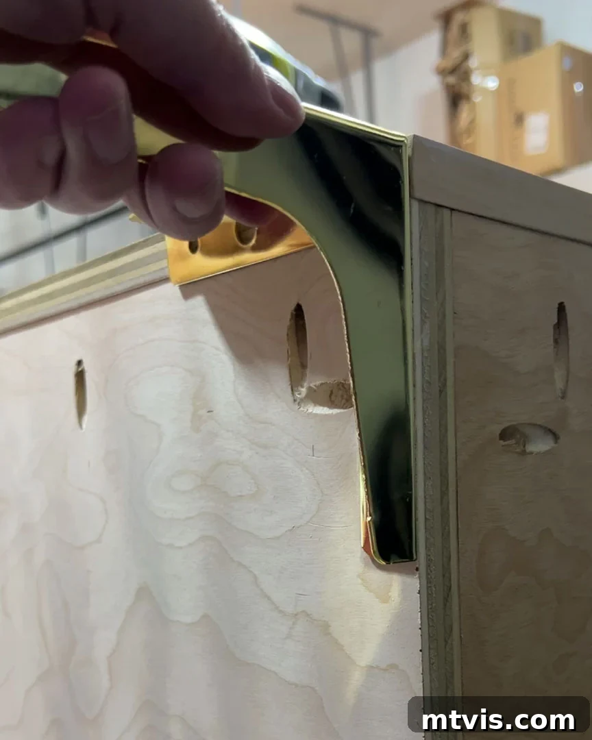Close-up photo of a person attaching gold furniture legs to the base of a DIY wooden dog crate, highlighting the installation process.