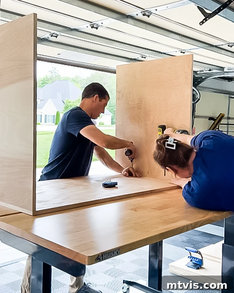 A man and woman collaborating to temporarily assemble the top and side panels of a DIY dog crate made from plywood, checking for fit before final assembly.