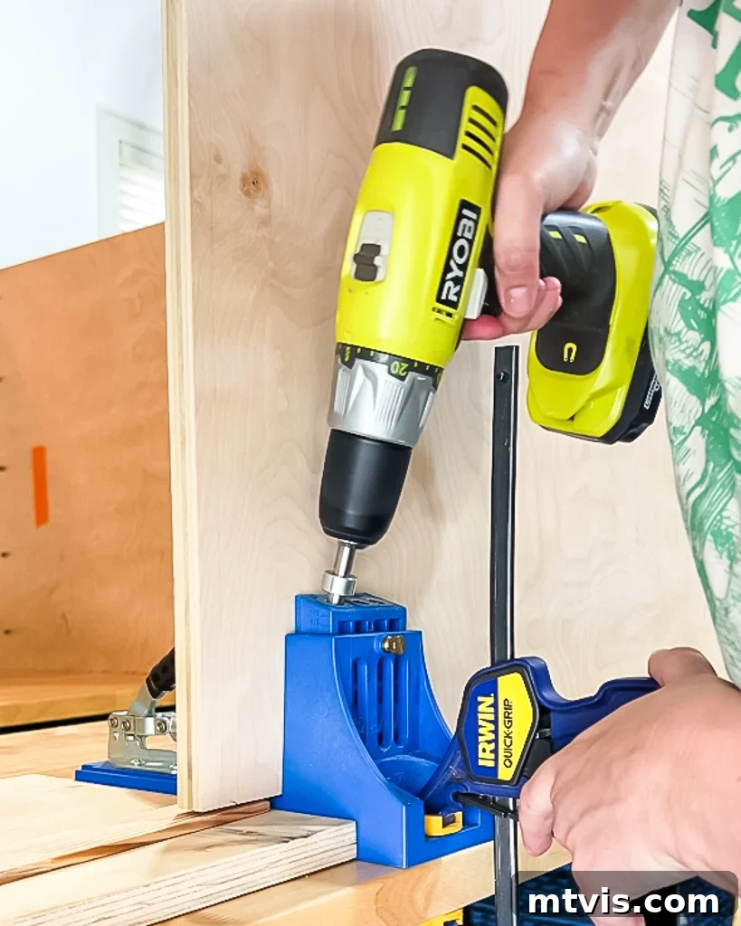 A close-up of a woman's hands using a Kreg jig to drill pocket holes into a piece of plywood, demonstrating preparation for assembling the DIY dog crate.