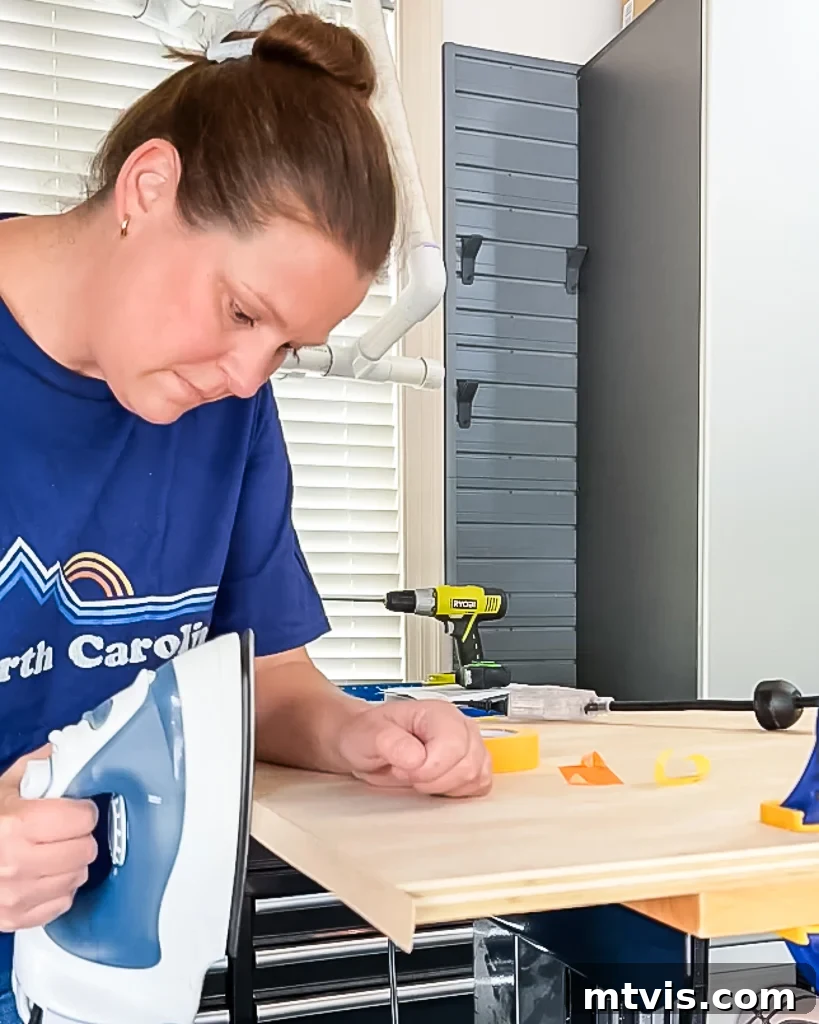 A woman meticulously ironing edge banding onto the exposed edges of a plywood piece, preparing it for a smooth, finished look in the DIY dog crate project.