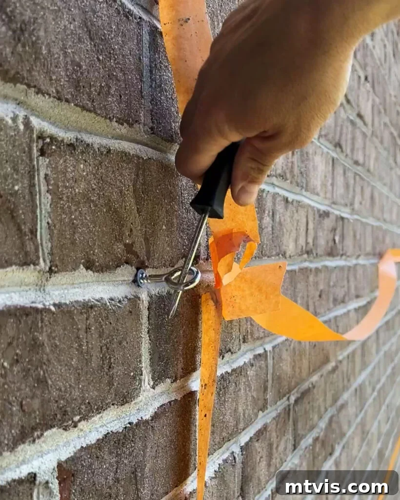 Man installing a screw eye hook into a brick wall for a DIY wire trellis, demonstrating the process