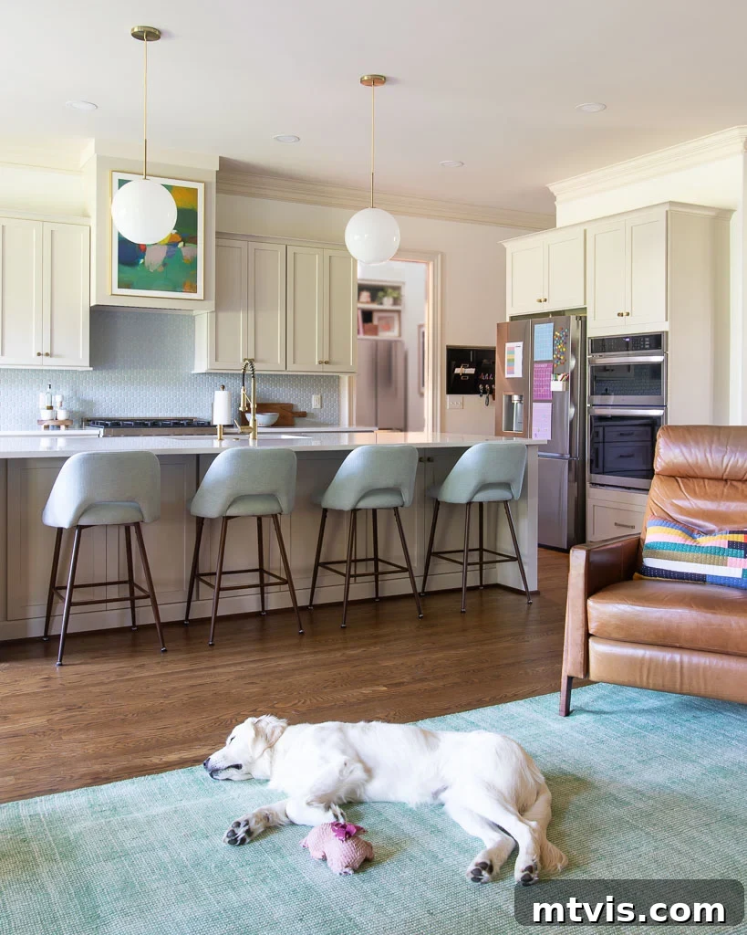 Our Kitchen Reveal: Serene Neutrals, Lively Hues 6 Photo of the redesigned great room, featuring a vibrant green rug, a comfortable leather recliner, and kitchen cabinets painted in Sherwin Williams Accessible Beige, demonstrating improved flow and aesthetic harmony.