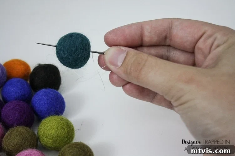 Homemade Pure Car Fragrance 4 A hand holds a needle that is piercing a deep blue felted ball used to make DIY car air fresheners.