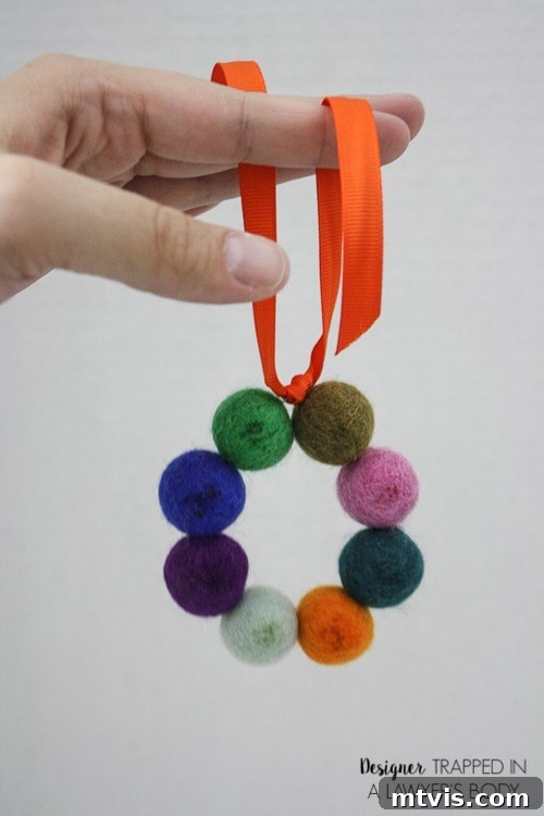 Homemade Pure Car Fragrance 9 A DIY car air freshener is held by a woman's hand. The scented craft is made from a circle of feted balls hung on an orange ribbon.