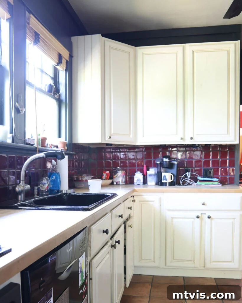 My Triple-Tested Method for Perfectly Painted Kitchen Cabinets 4 photo of outdated kitchen with red tile backsplash, black walls and damaged cream colored cabinets before renovation