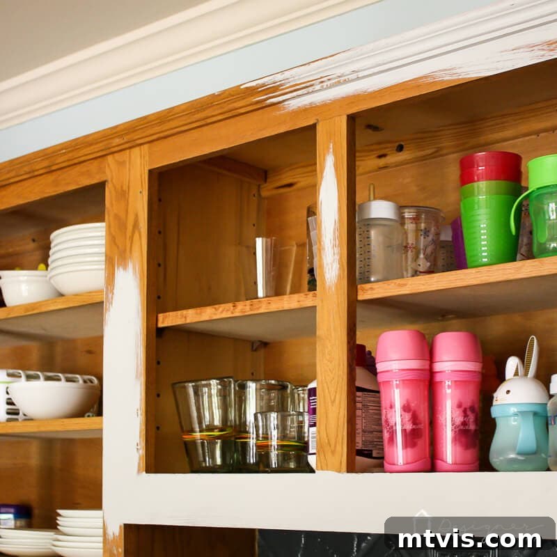 My Triple-Tested Method for Perfectly Painted Kitchen Cabinets 9 photo of the frame of natural oak kitchen cabinet boxes being painted a light gray color with contents of kitchen cabinets still in place, demonstrating in-situ painting