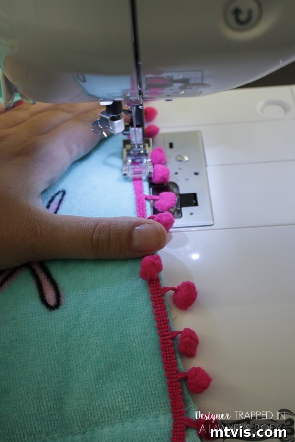 Sewing colorful pom-pom trim onto a child's DIY towel cover-up for a playful touch.
