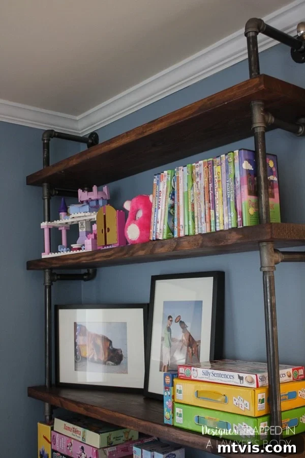 Industrial Chic: DIY Pipe Shelves and Integrated Workspaces 14 Close-up of a section of the finished pipe shelves filled with books and toys, demonstrating practical storage in the playroom.