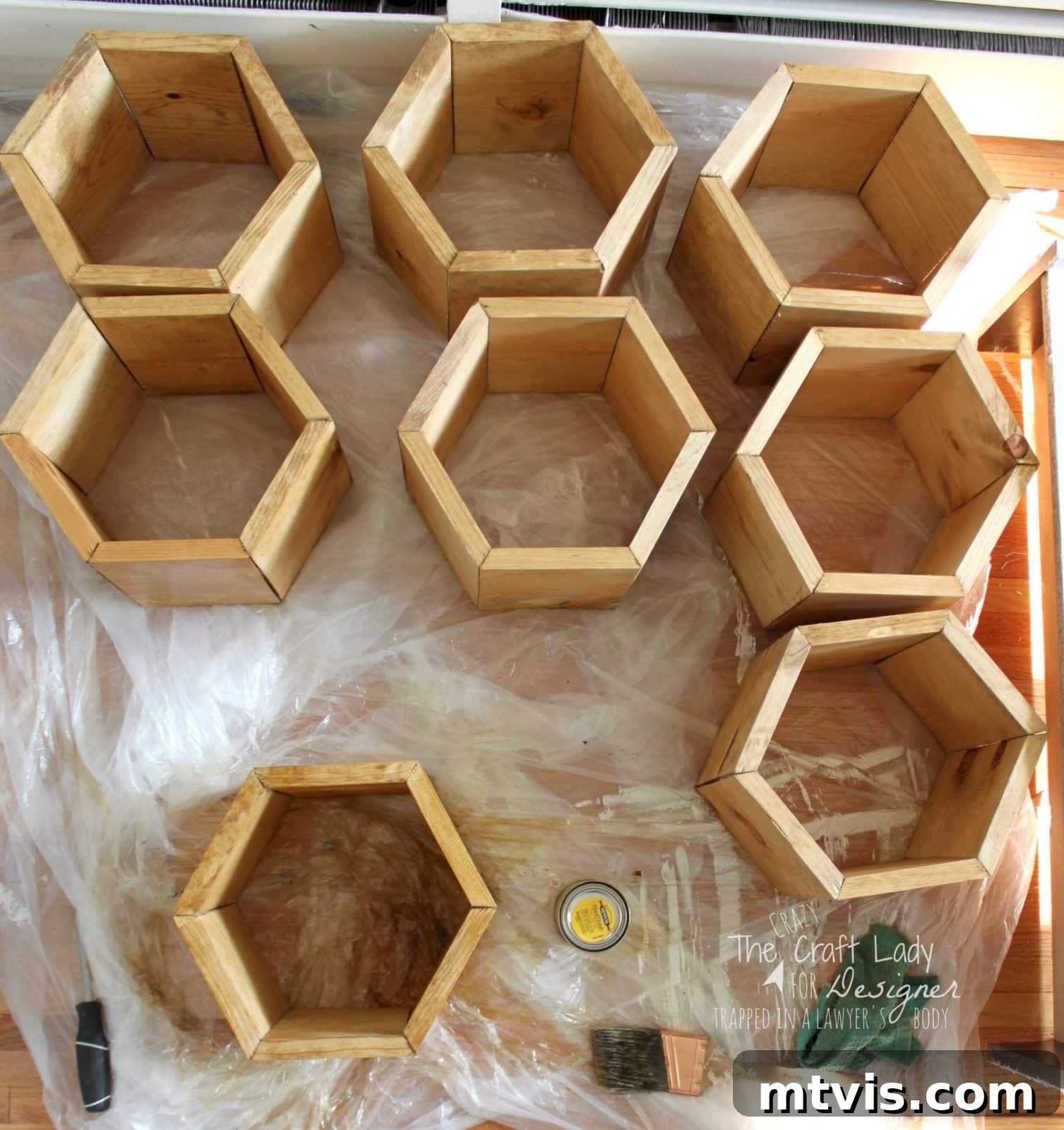 Honeycomb Shoe Organizer 15 Hexagon-shaped wooden shoe cubbies laid out on a plastic-covered hard wood floor, ready for staining or sealing, with a brush, screwdriver, and wood finish can nearby. Text in the lower right corner reads,