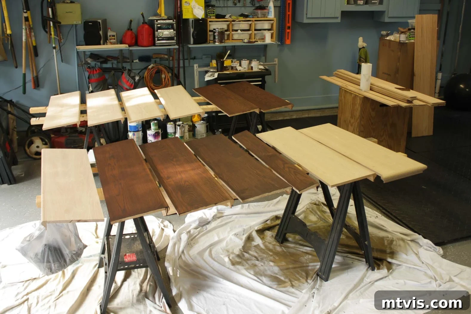 Person applying wood stain to new hardwood stair treads on sawhorses, preparing them for installation