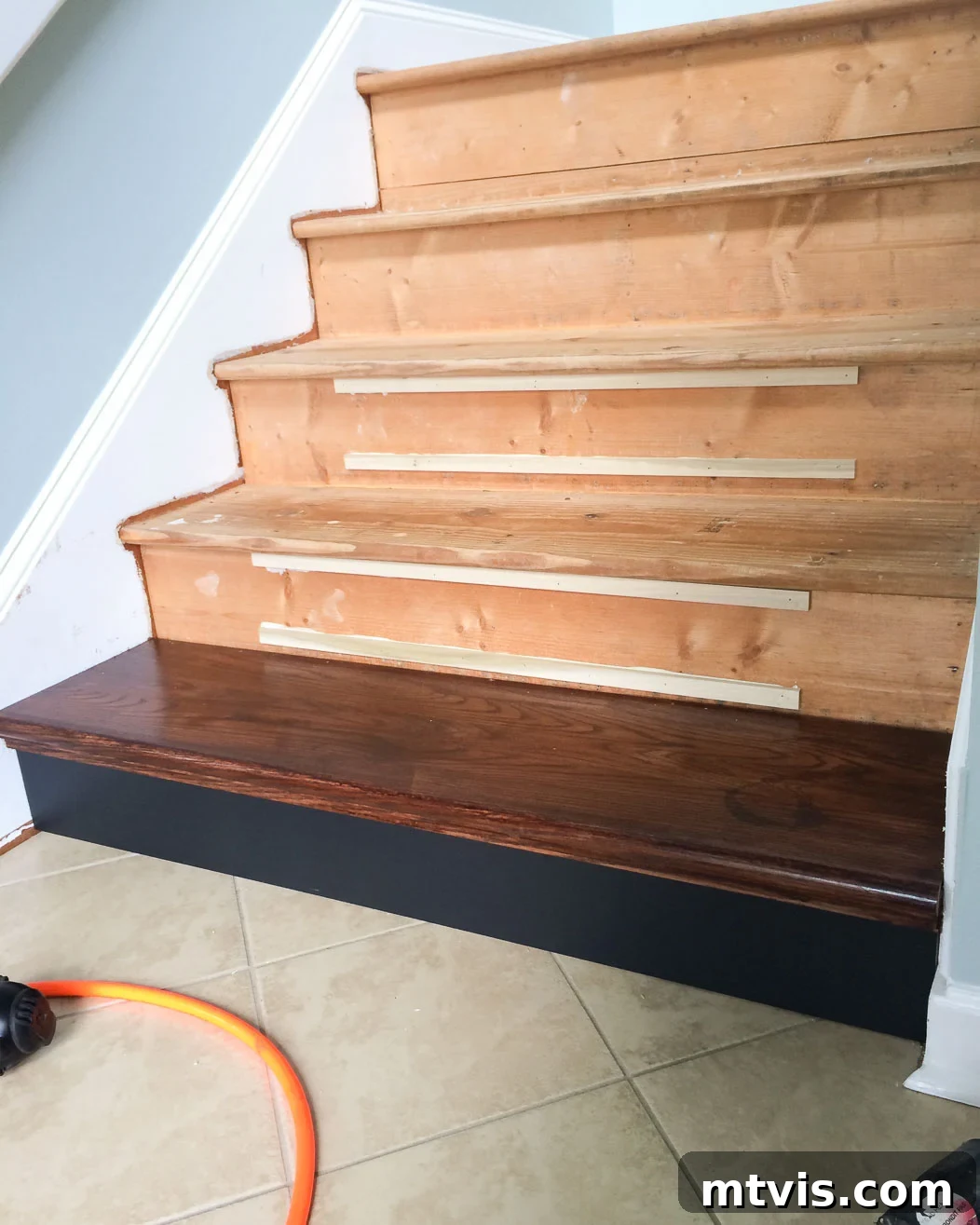 Close-up of the first DIY hardwood stair tread and riser installed, showing shims for subsequent steps